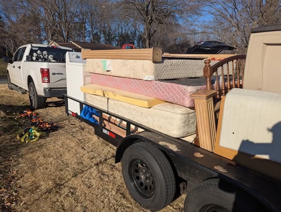 Mattresses, appliances, and bed frames stacked on the dump trailer for transport.